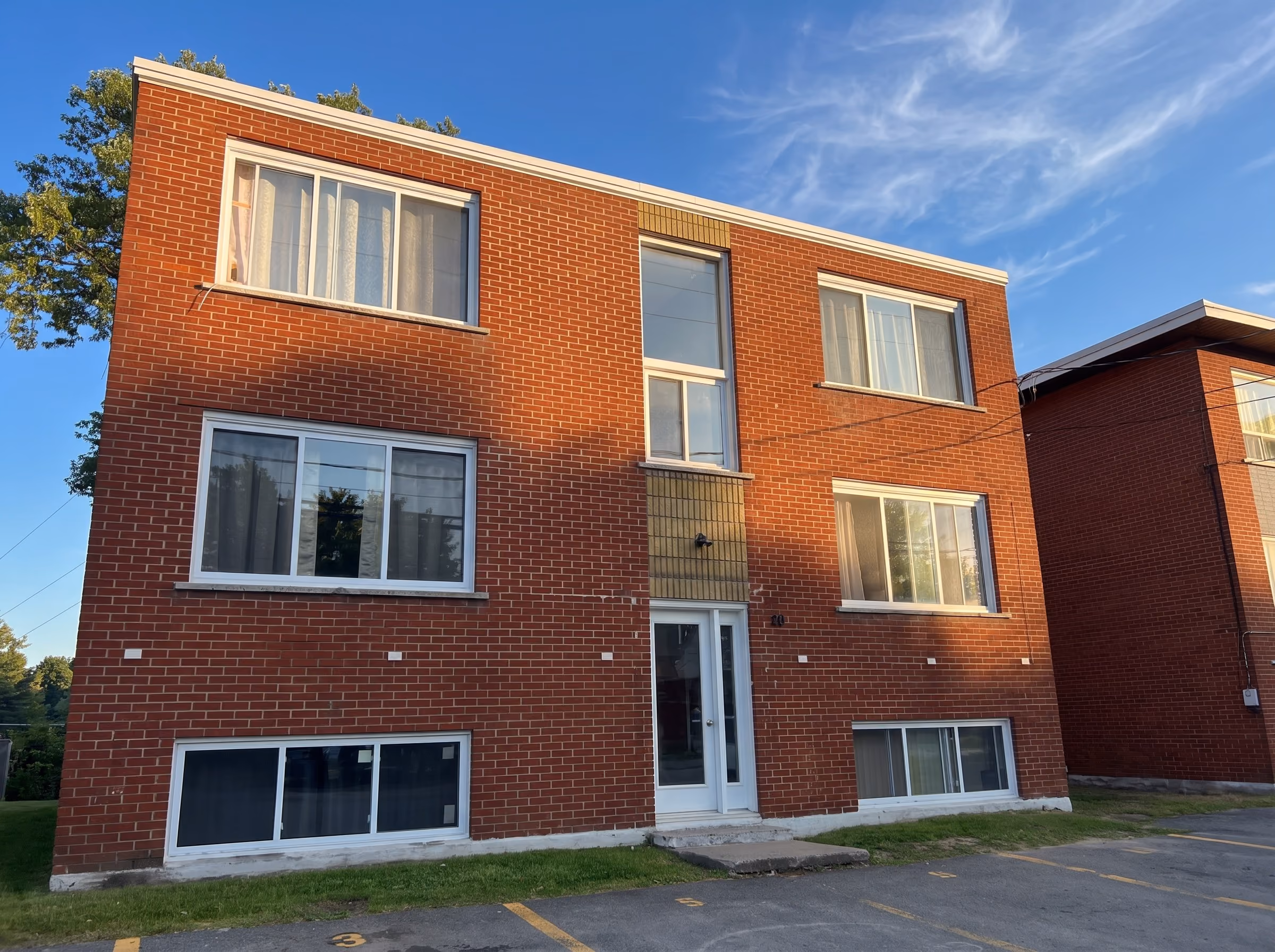 Three-storey red brick building with new white windows, late-afternoon blue sky.
