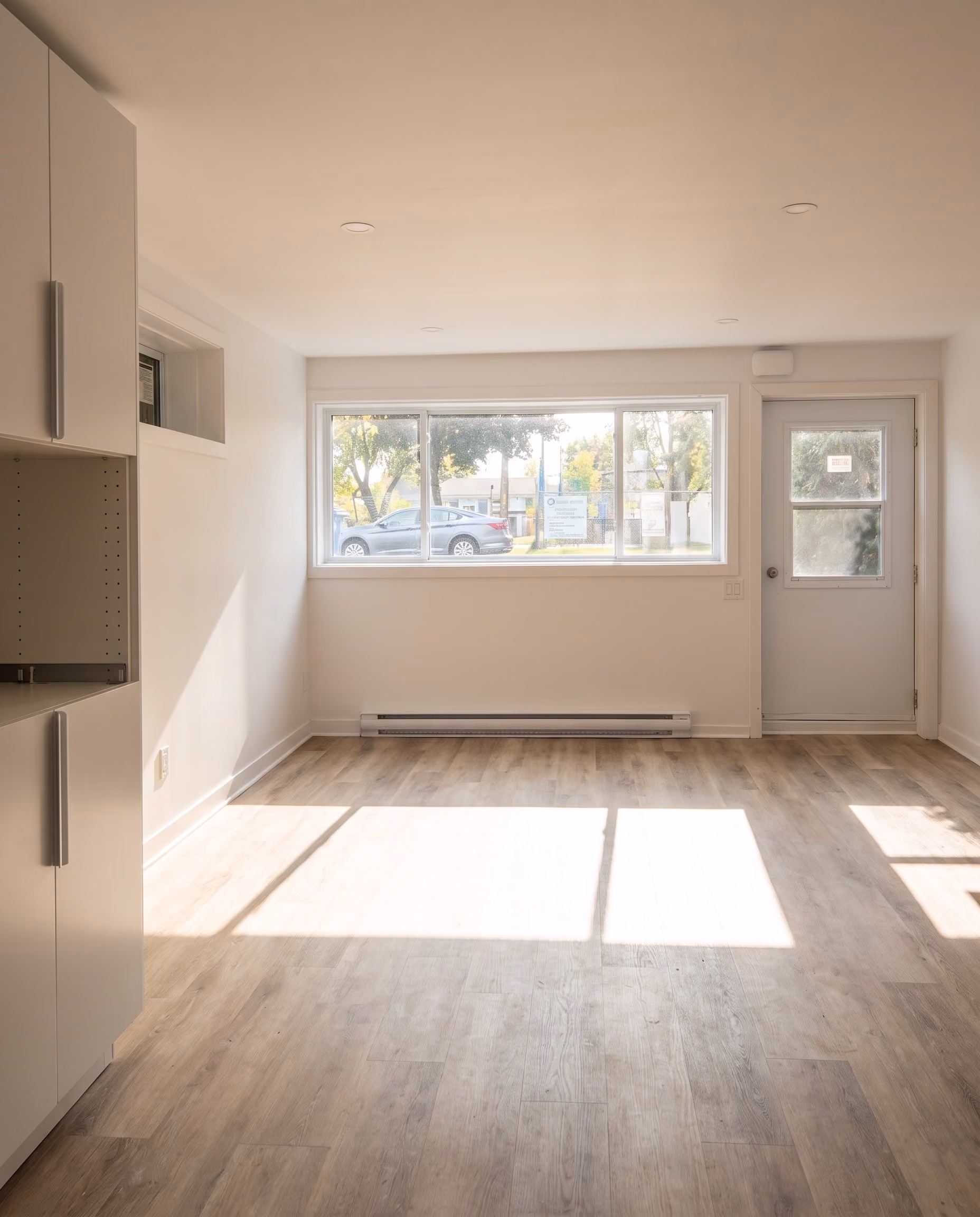 Freshly renovated empty room with a large window and a glazed door, light wood floor.