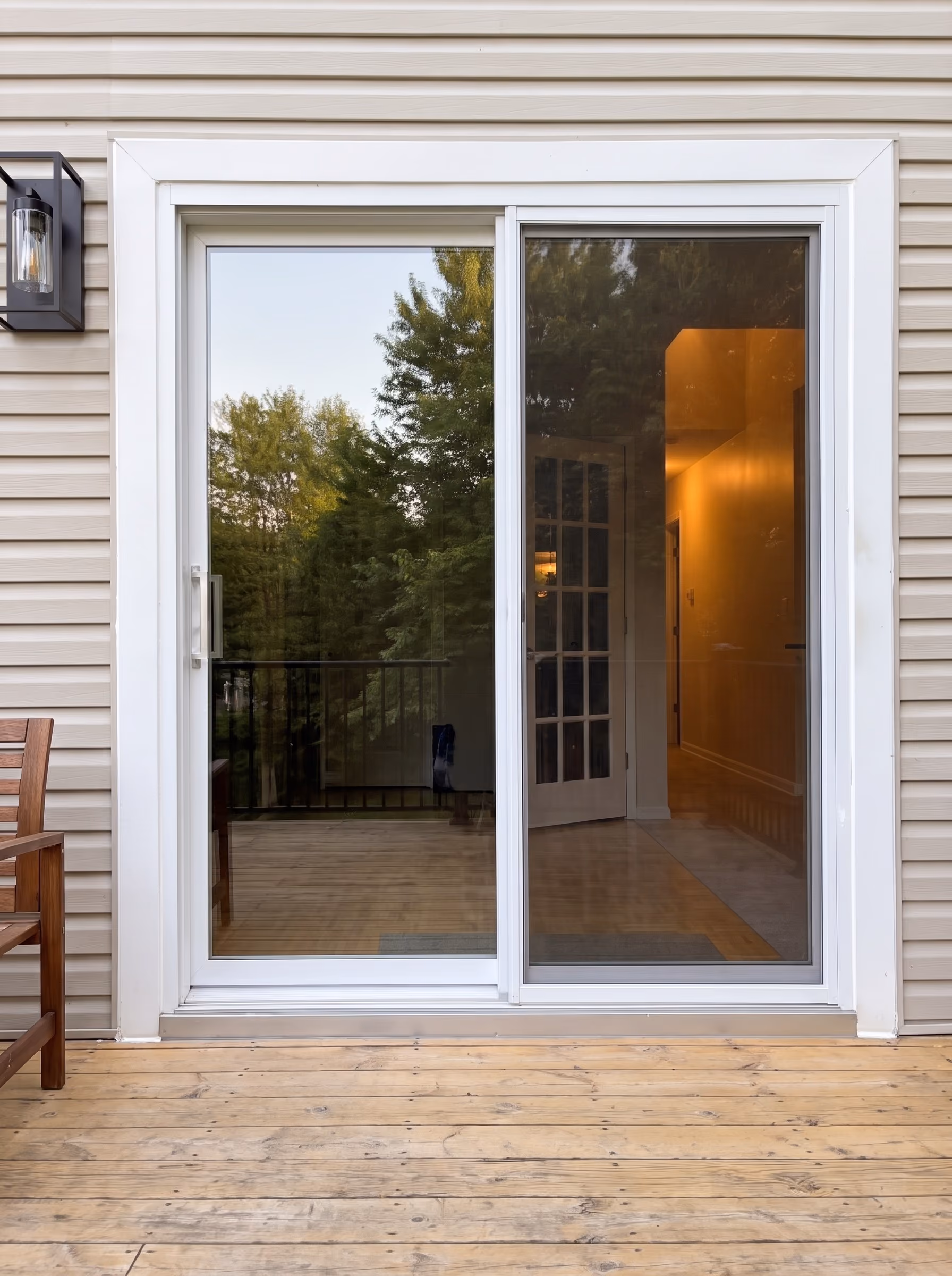 White-framed sliding patio door on a wood deck, the lit interior visible through the glass.
